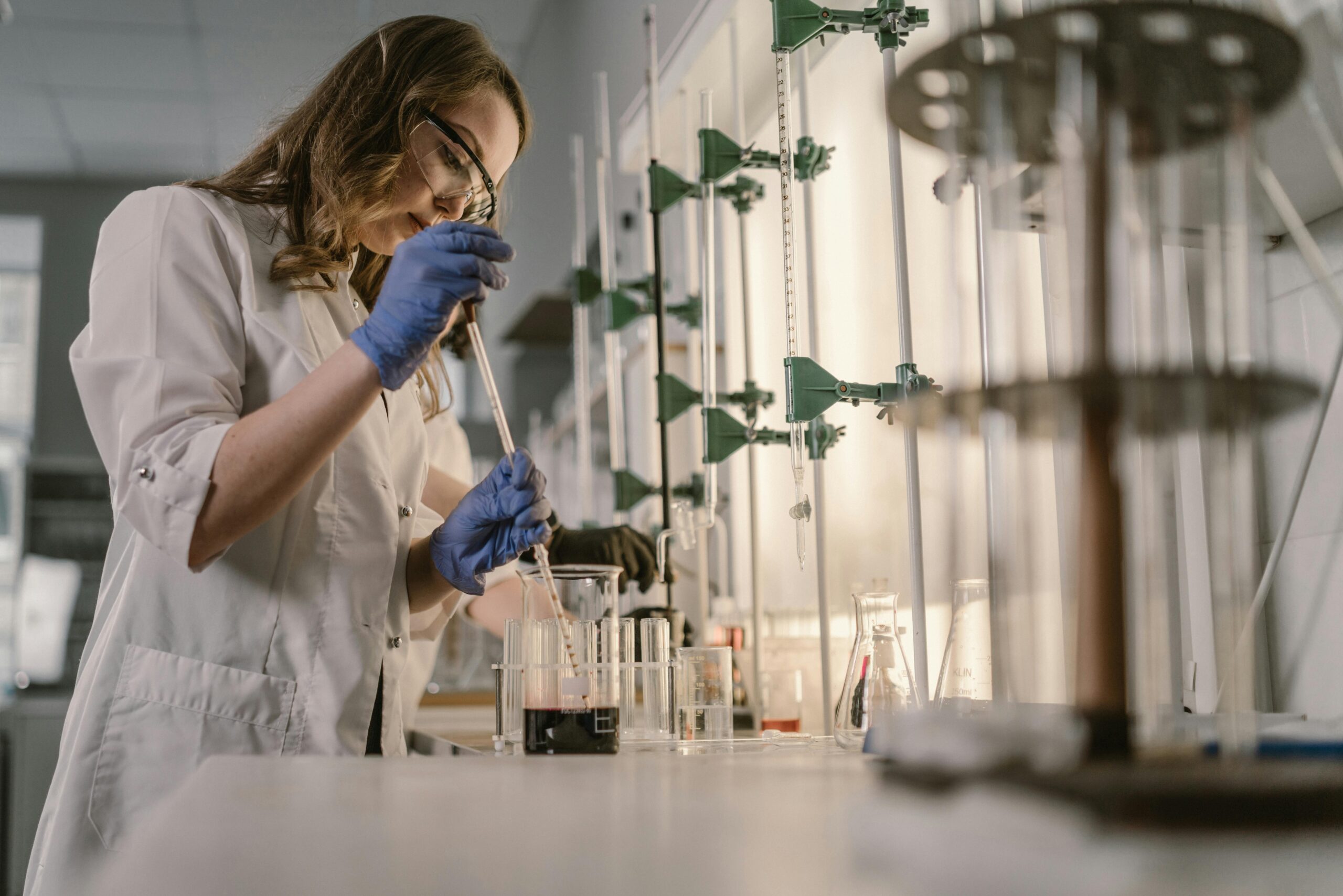 Female scientist performing an experiment in a laboratory setting with lab equipment and safety gear.